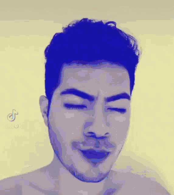 a shirtless man with blue hair and a beard is making a funny face with his eyes closed .