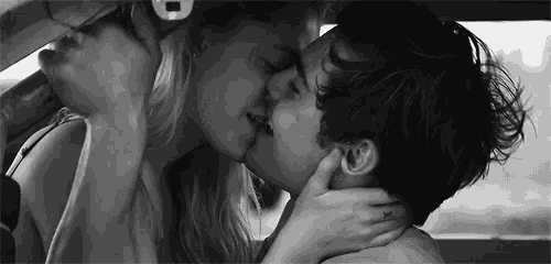 a man and a woman are kissing in a car in a black and white photo .
