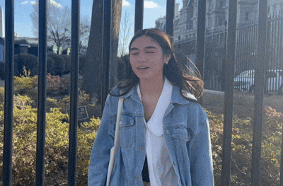 a woman in a denim jacket stands in front of a fence with a sign that says no parking
