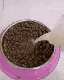 a bowl of dog food is being poured into a pink bowl .