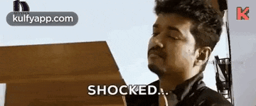 a man with a beard is sitting in front of a laptop and saying `` shocked `` .