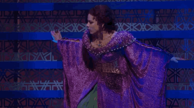 a woman in a purple dress is dancing in front of a blue wall