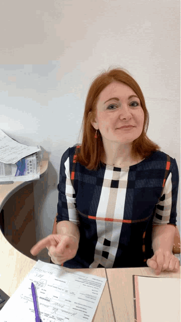 a woman in a plaid shirt sits at a desk with a pen and paper