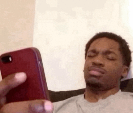 a man is sitting on a couch looking at his cell phone and making a funny face .