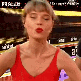 a woman in a red tank top is making a funny face in front of an antel sign