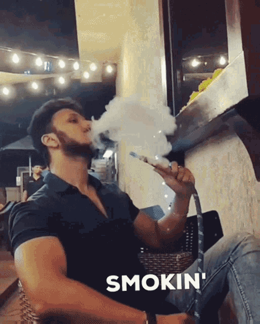 a man in a black shirt is smoking a hookah and the word smokin is above him