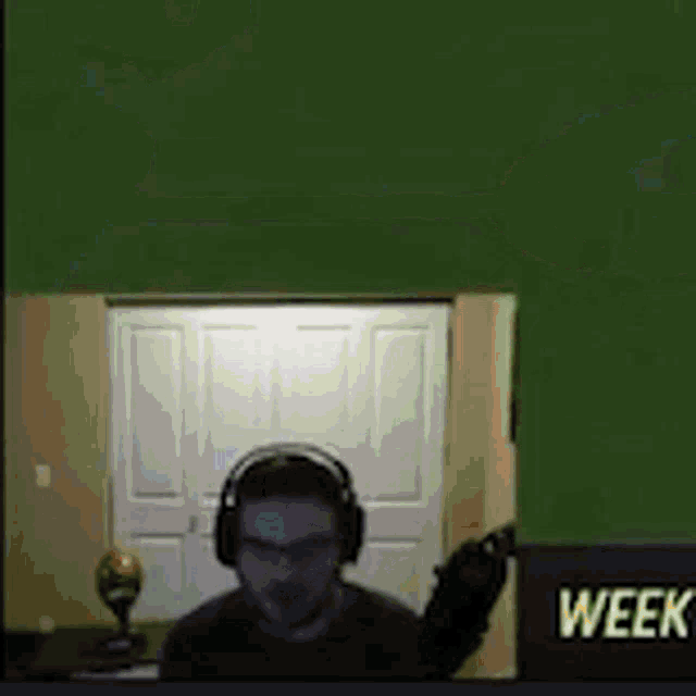 a man wearing headphones is sitting in front of a green wall with the word week on it .