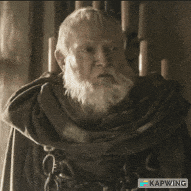 a man with a beard is sitting in a chair and looking at a piece of paper that says kapwing