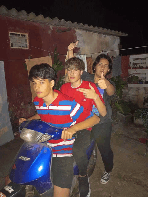 three young men are posing for a picture on a blue scooter with a sticker that says ' rs ' on it