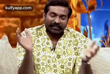 a man with a mustache and a green shirt is sitting on a couch with his hands outstretched .