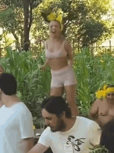 a woman in a bikini top and shorts is standing on a man 's shoulders in a field .