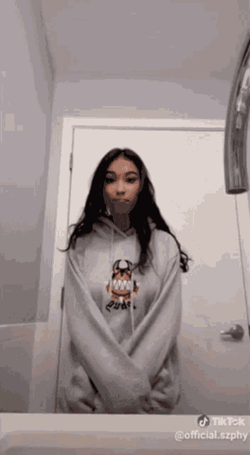 a woman in a hoodie stands in front of a door with a watermark that says tik tok