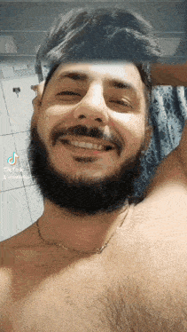 a shirtless man with a beard is smiling for the camera and has a tiktok sticker on his face