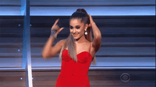 ariana grande is wearing a red dress and making a peace sign with her hands .