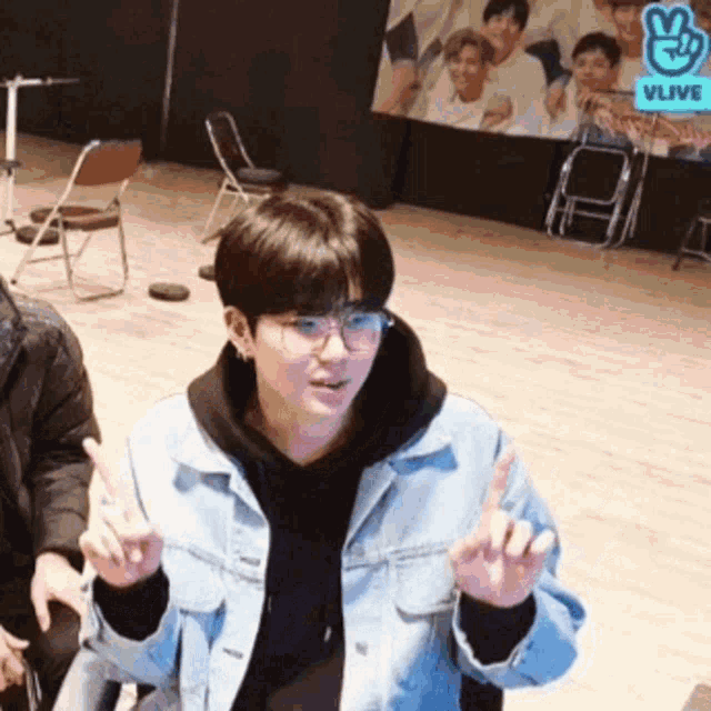 a boy wearing glasses and a denim jacket is giving a peace sign
