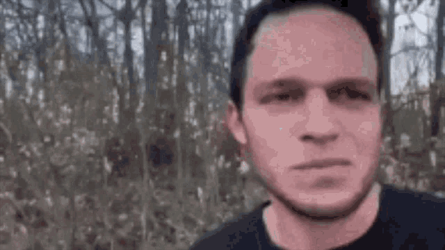 a man in a black shirt is standing in front of a forest .