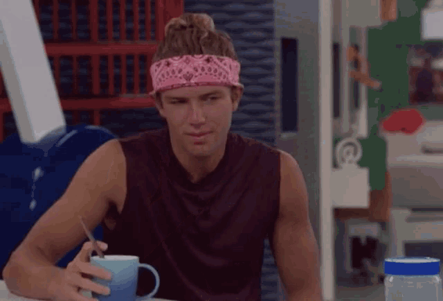 a man wearing a pink bandana holds a blue mug