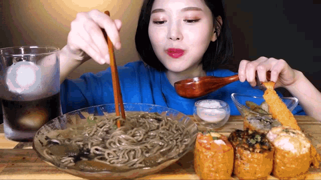 a woman in a blue shirt is eating noodles and sushi