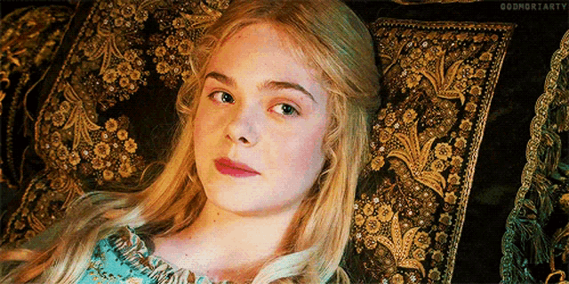 a woman with blonde hair is laying on a couch with a gold pillow .