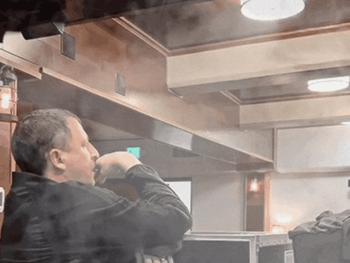 a man in a black jacket is smoking a cigarette in a restaurant