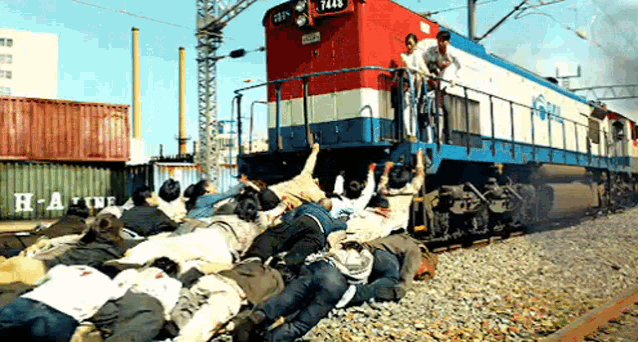 a group of people are laying on the tracks in front of a train with the number 7448 on the front