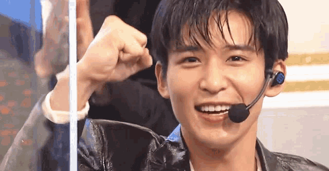 a young man wearing a microphone and headphones is smiling and making a fist .