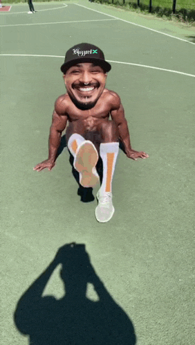 a shirtless man wearing a hat that says ' blissyard ' on it sits on a basketball court