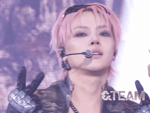a woman with pink hair is wearing a microphone and gloves and the word team is on the bottom right