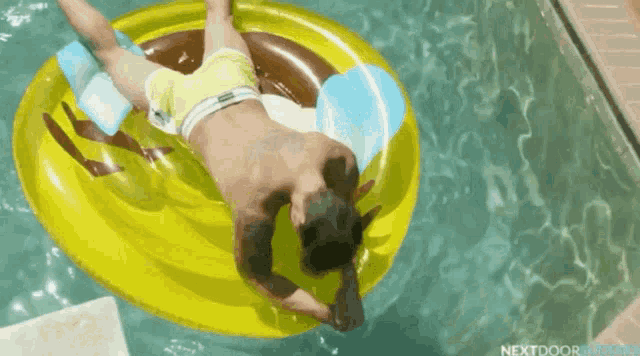 a shirtless man is laying on a yellow raft in a pool .