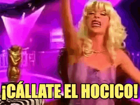 a woman in a blonde wig is sitting in a chair with her arms in the air and says callate el hotico .