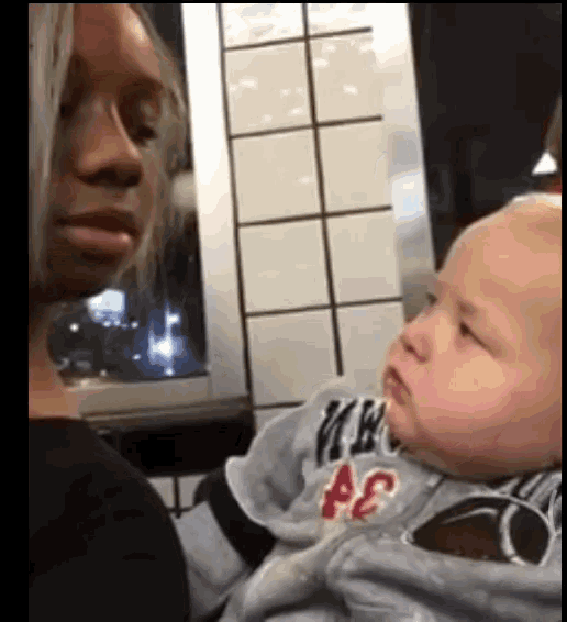 a woman is holding a baby who is wearing a sweater with the letter ae on it