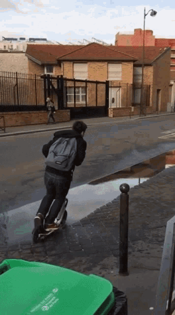 a person riding a scooter down a street with a green trash can in front of them