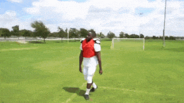 a man is walking on a soccer field wearing a red vest .