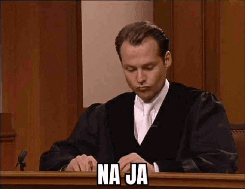 a man in a judge 's robe is sitting at a judge 's bench with the words na ja above him .