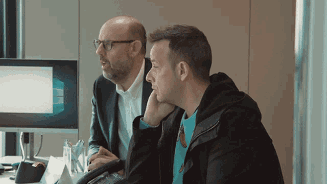 two men are sitting in front of a computer screen with a windows logo on it