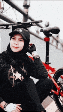 a woman wearing a black hat with a skull and crossbones on it sits next to a red bicycle