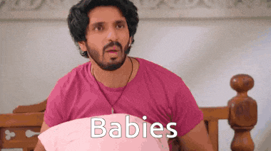 a man in a pink shirt is laying on a bed with a pillow and the word babies written on it