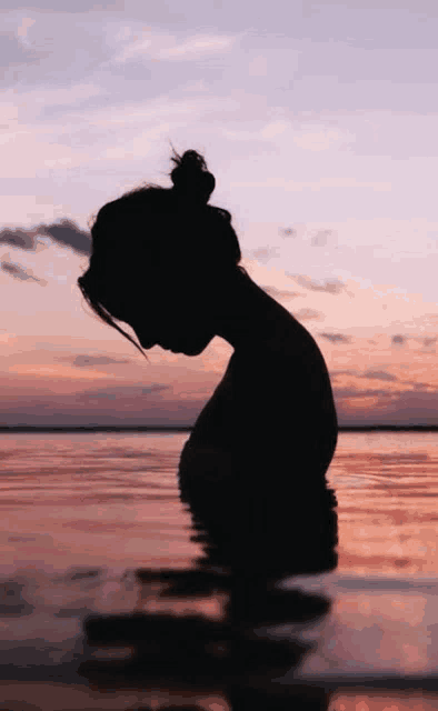a woman is standing in the water at sunset with her head in the water .