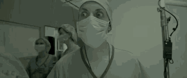 a female surgeon wearing a surgical mask and a surgical cap is standing in a hospital hallway .