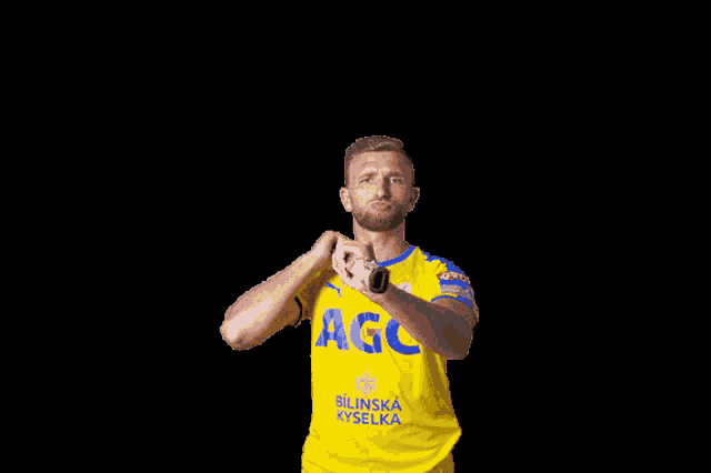 a man in a yellow agc shirt holds a tennis racket