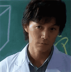 a man wearing a white lab coat is standing in front of a blackboard .