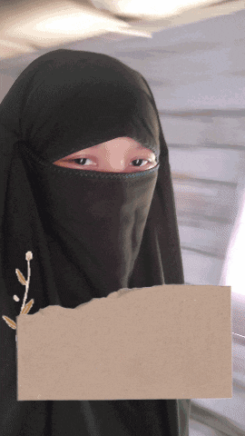 a woman wearing a black hijab holds a piece of paper in front of her face