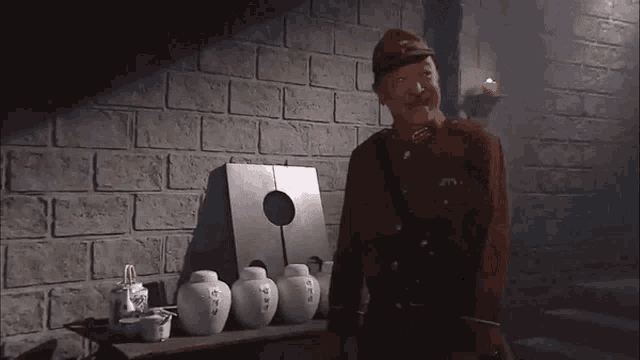 a man in a military uniform is standing in front of a brick wall and a table with jars on it .
