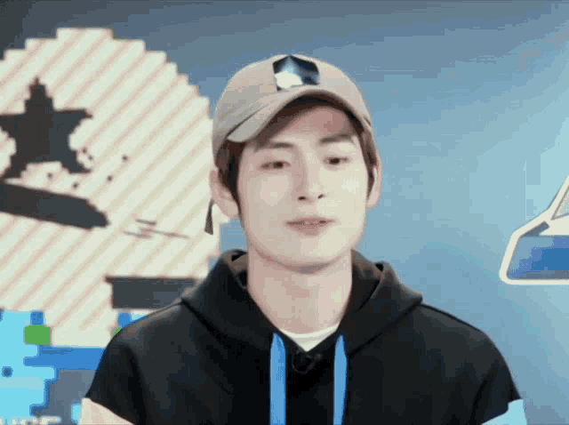 a young man wearing a baseball cap and a hoodie looks at the camera