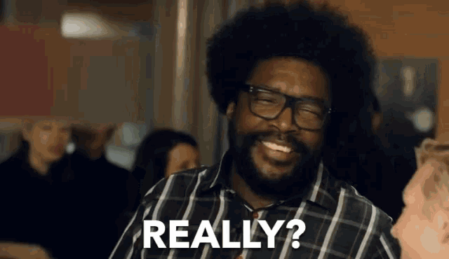 a man with glasses and a beard is smiling and says really