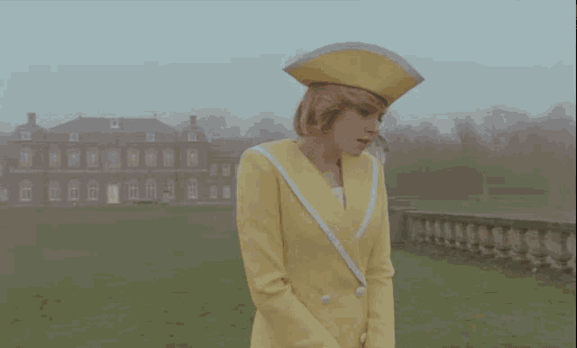 a woman in a yellow suit and hat is standing in front of a building