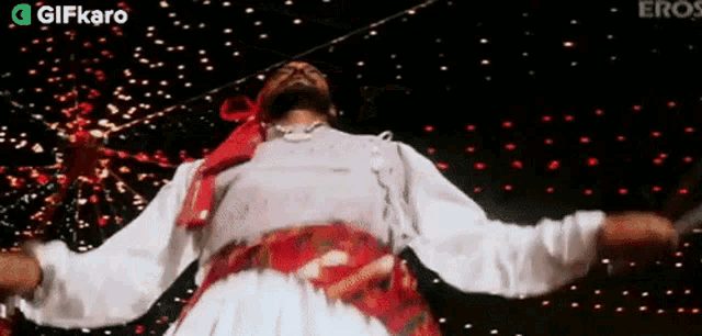 a man in a white shirt and red sash is dancing in front of a crowd .