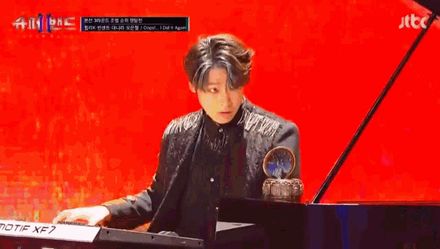 a man in a black jacket is playing a piano on a stage .