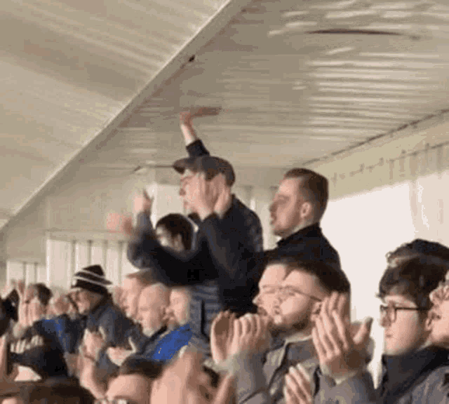 a group of people are sitting in a stadium watching a game and clapping their hands .