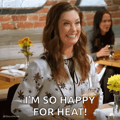 a woman is sitting at a table with a glass of beer and smiling while saying i 'm so happy for heat !